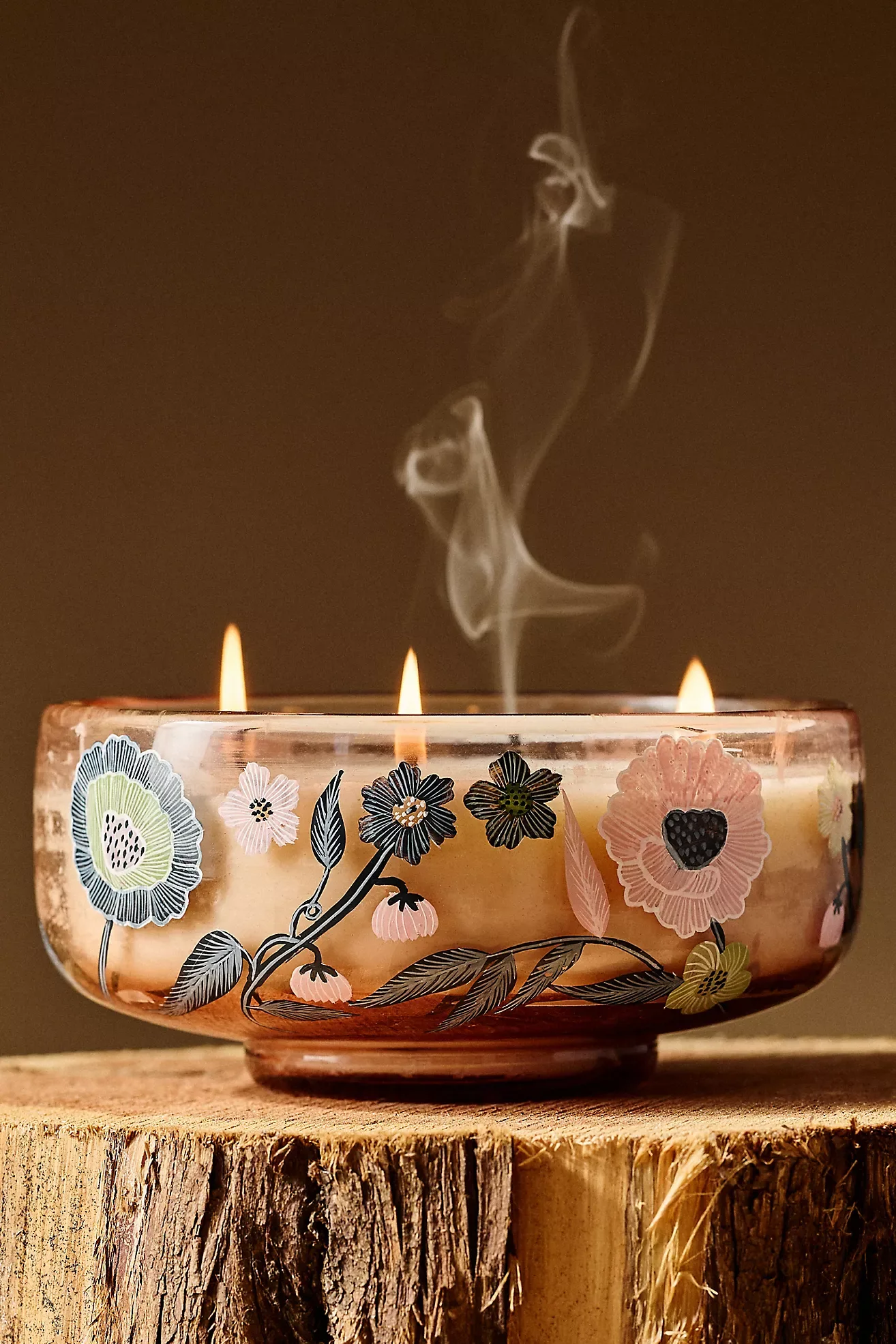 Three-wick floral glass candle burning on a rustic wood surface
